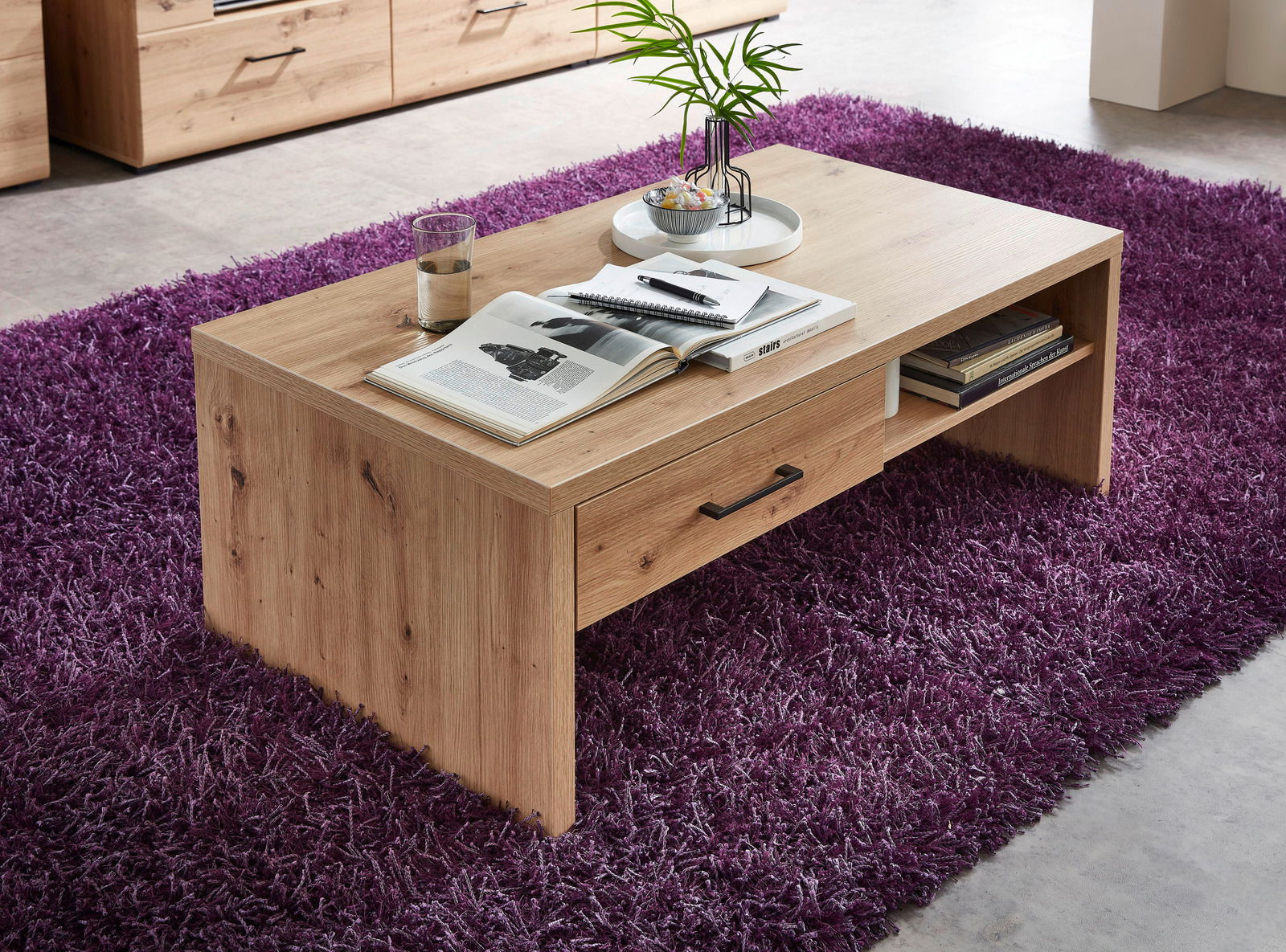 Moderner Couchtisch aus Holz mit Schublade und Ablagefach, auf lila Teppich, aus seitlicher Perspektive fotografiert.