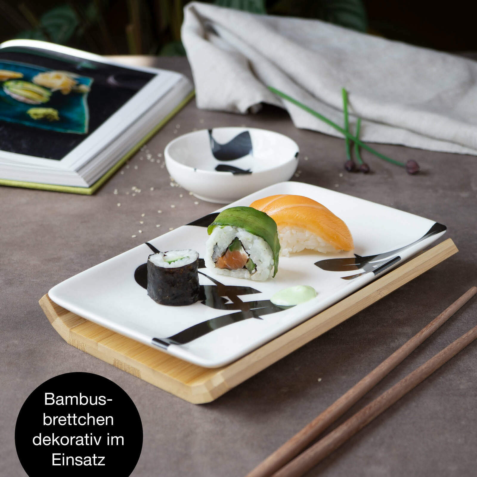 Sushi-Set mit dekorativem Bambusbrettchen, Teller und Schale mit schwarzer Schrift, von oben fotografiert.