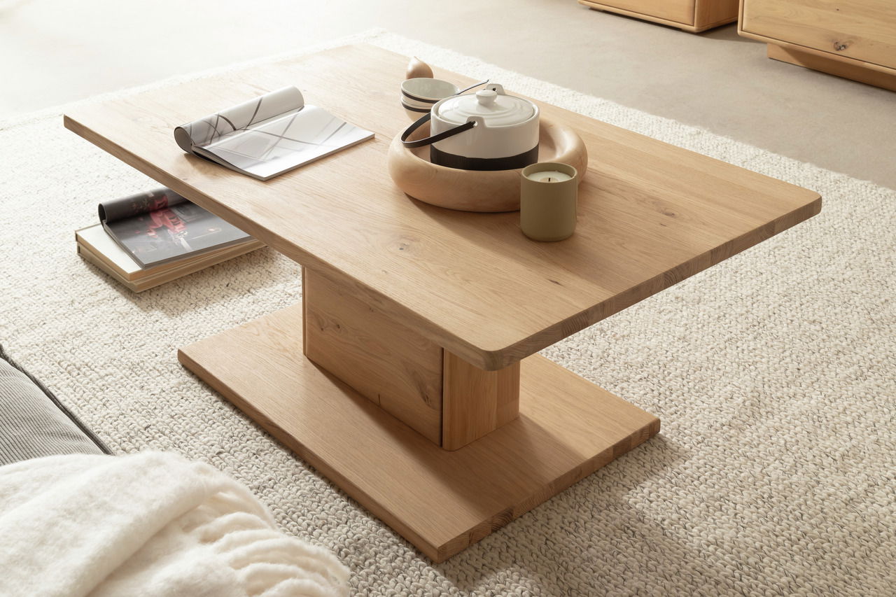 Moderner Couchtisch aus Holz in seitlicher Perspektive, dekoriert mit einer Teekanne, Kerze und Zeitschriften auf einem hellen Teppich.