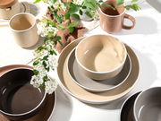 Kombiservice 16-tlg. in natürlichen Erdtönen, bestehend aus Tassen, Schalen und Tellern, auf einem Tisch mit Blumenarrangement, aus der Vogelperspektive fotografiert.