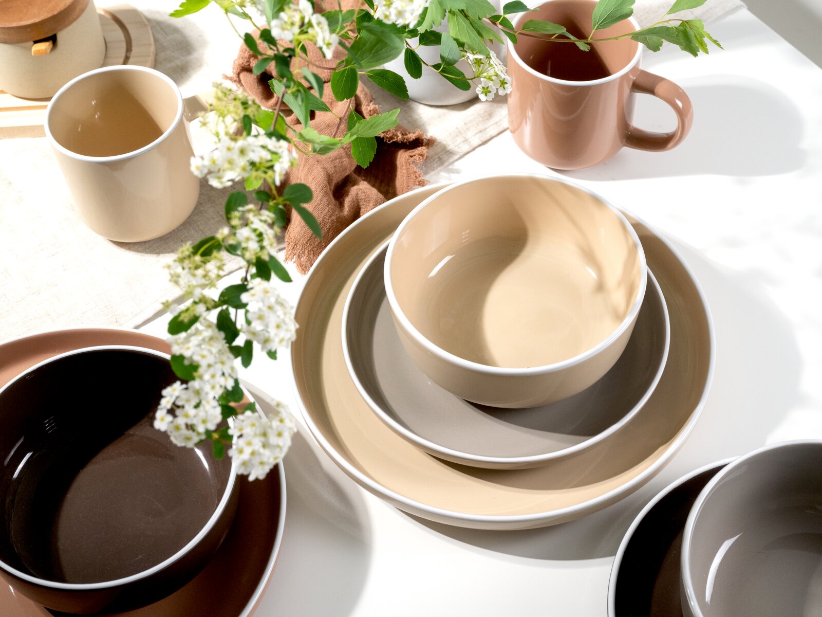 Servies 16-delig in natuurlijke aardetinten, bestaande uit kopjes, schalen en borden, op een tafel met een bloemstuk, gefotografeerd vanuit vogelperspectief.