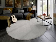 Runder, hellgrauer Uni-Teppich in einem modernen Wohnzimmer mit dunklem Sofa, Gitarre und Couchtisch. Perspektive von oben.