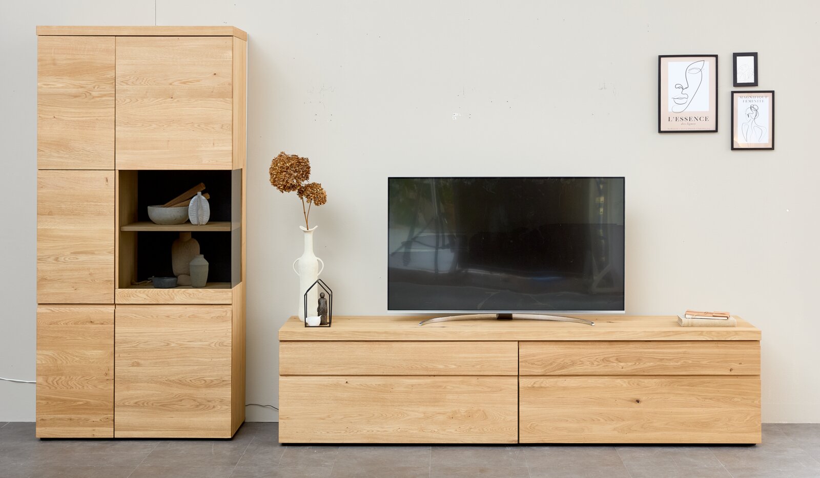 Moderne Wohnwand aus hellem Naturholz mit hohem Vitrinenschrank und breitem TV-Lowboard, frontal in einem stilvoll dekorierten Wohnzimmer dargestellt.