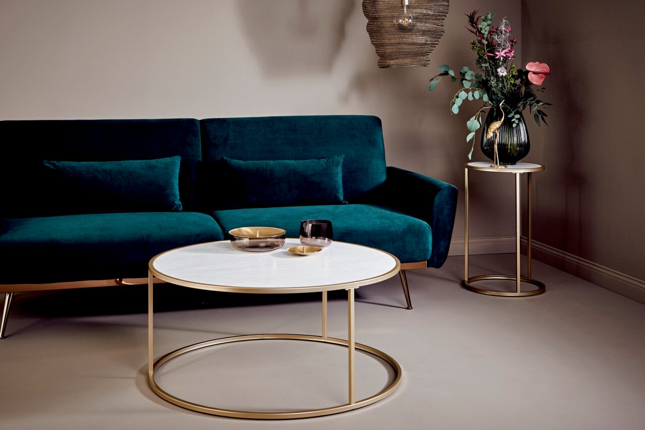 Jahnke Couchtisch SOL Moderner Couchtisch mit rundem, weißem Marmor-Tischplatte und goldfarbenem Metallgestell, im Vordergrund einer stilvollen Wohnzimmerumgebung mit grünem Sofa, seitliche Perspektive.