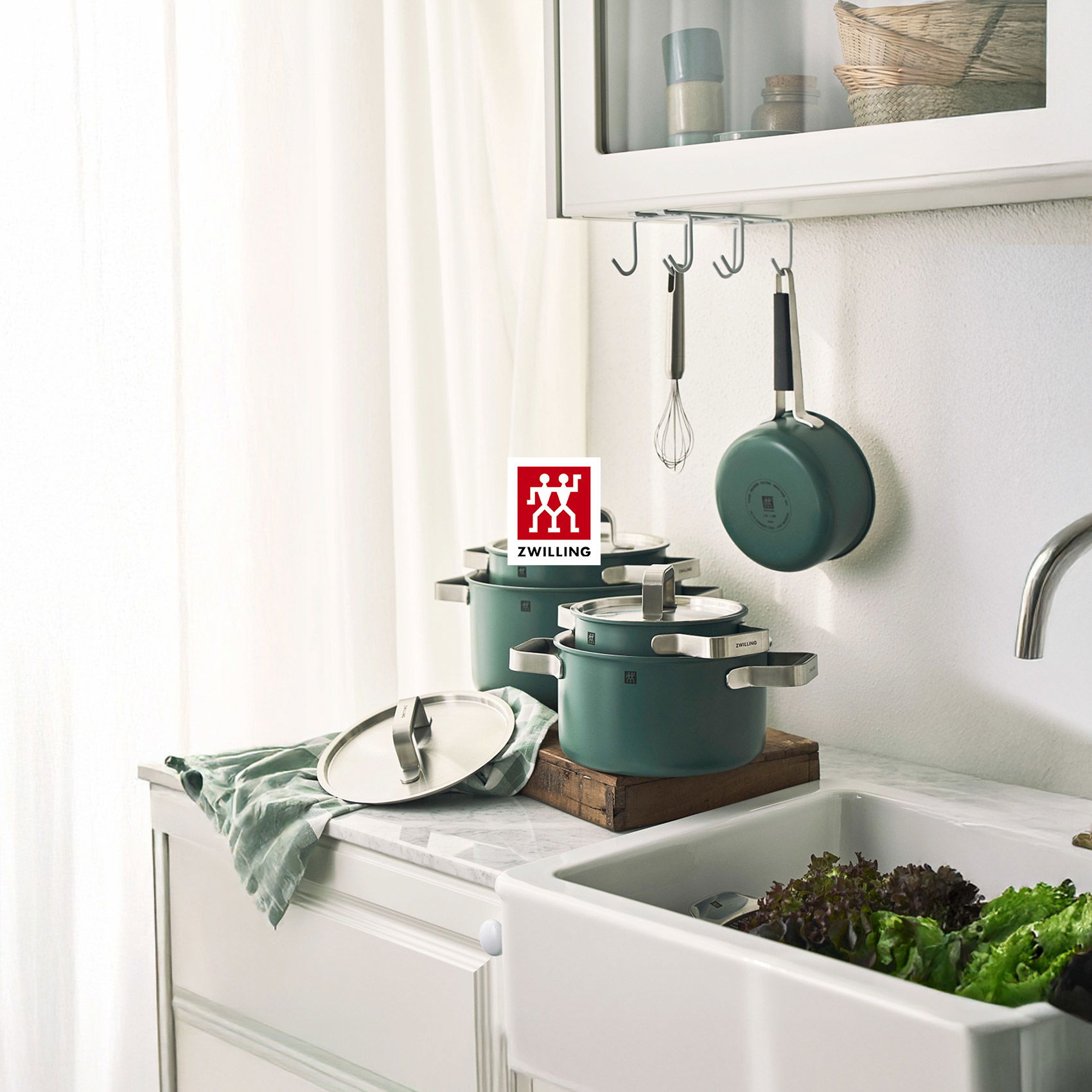 Helle, minimalistische Küche mit weißen Schränken, Spüle und grünem Kochgeschirr in ruhiger Atmosphäre.