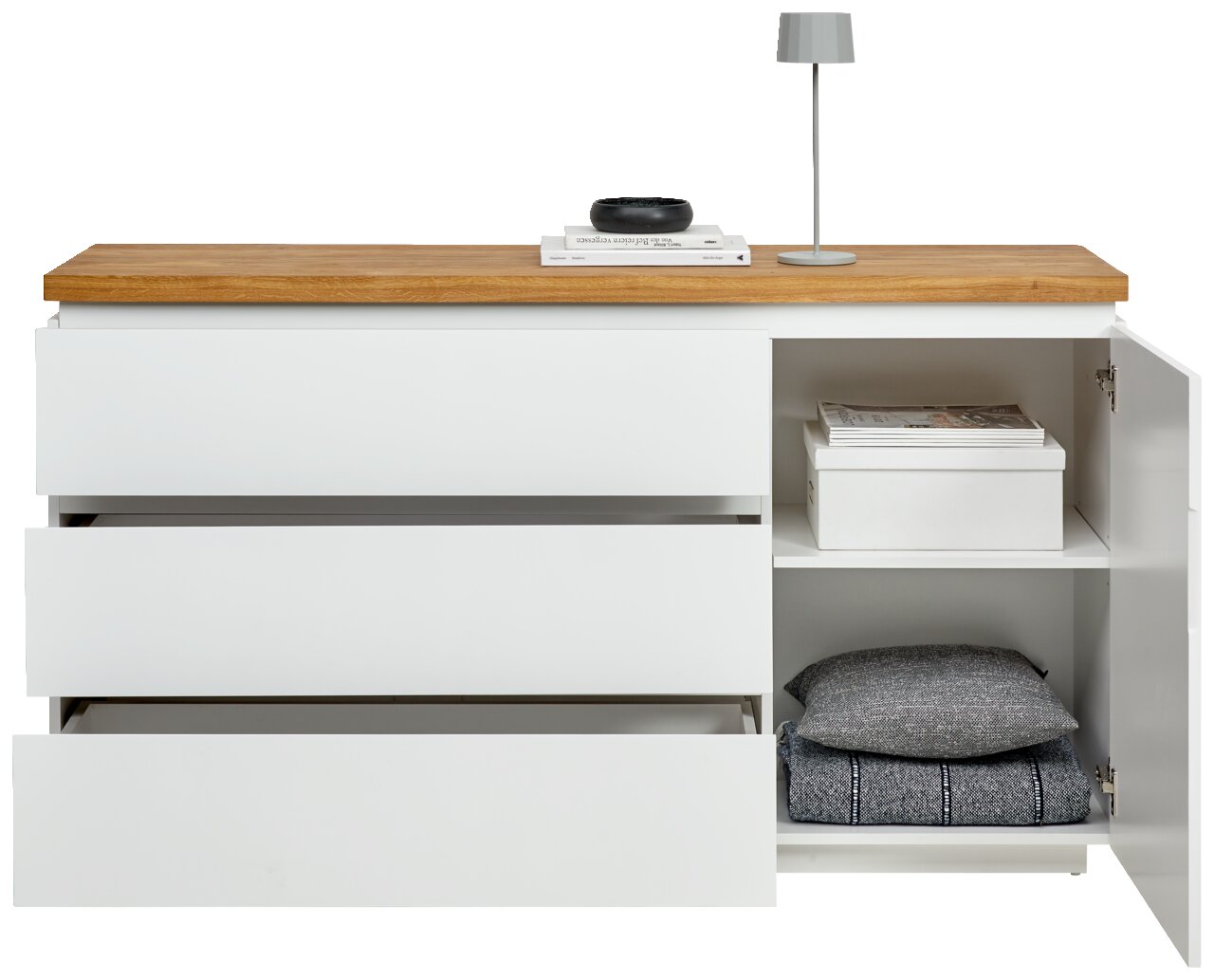 Weißes Sideboard mit drei offenen Schubladen und einem offenen Schrankfach, darauf eine Lampe und Bücher, frontale Ansicht