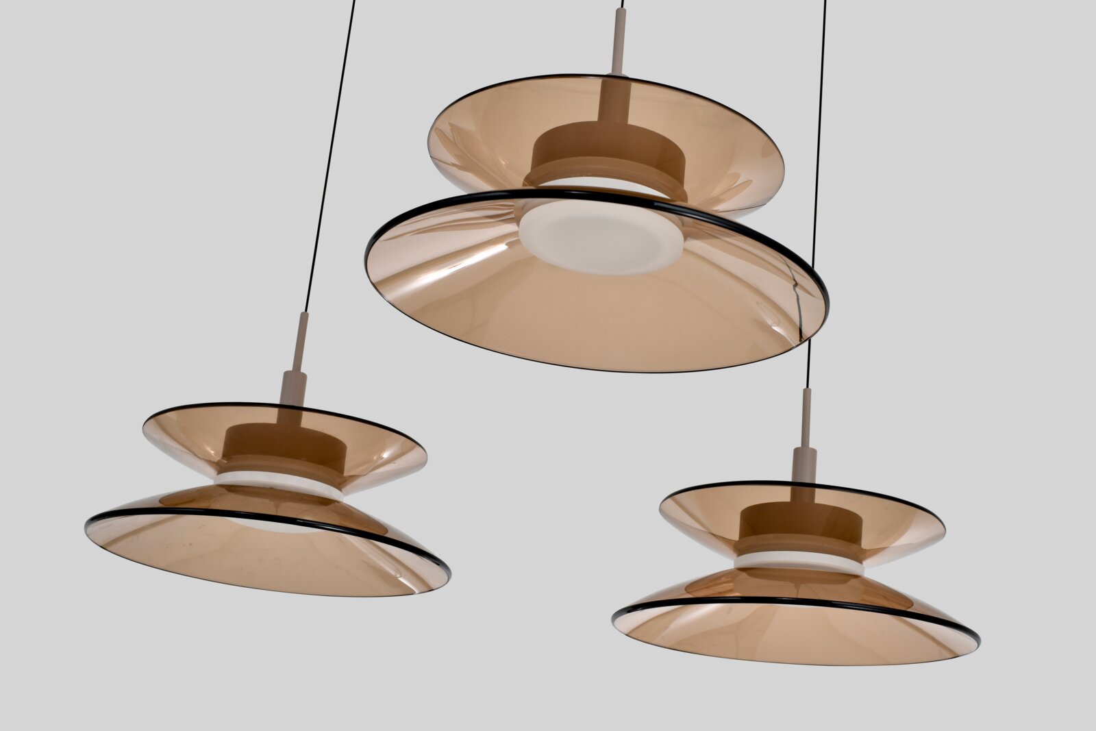 Drie moderne hanglampen met dubbele schijven van amberkleurig transparant glas en witte lichtdiffuser, vanuit onderaanzicht tegen een lichtgrijze achtergrond