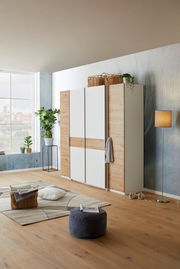 Moderner Dreh-Schwebetürenschrank mit vier Türen in Holzoptik und weißen Elementen, seitliche Perspektive im stilvoll eingerichteten Raum.