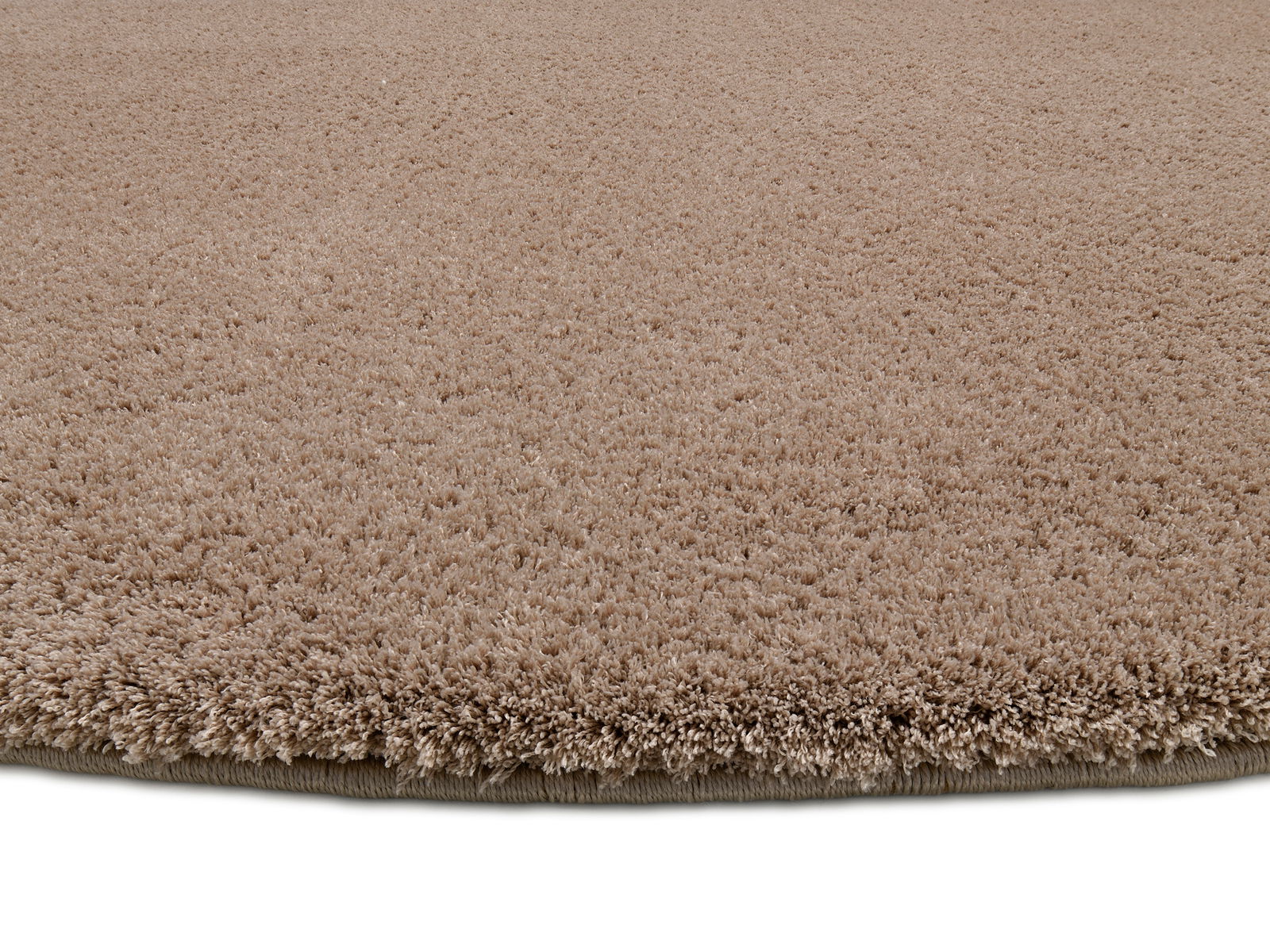 Nahaufnahme eines runden, beigen Teppichs mit weicher, flauschiger Textur, seitliche Perspektive.