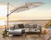 Heller Ampelschirm mit seitlichem Mast über einer modernen Outdoor-Lounge am Strand bei Sonnenuntergang, Perspektive: leicht seitliche Ansicht von vorn.