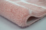 Nahaufnahme eines flauschigen, rosa Badteppichs mit weißem Muster, seitliche Perspektive