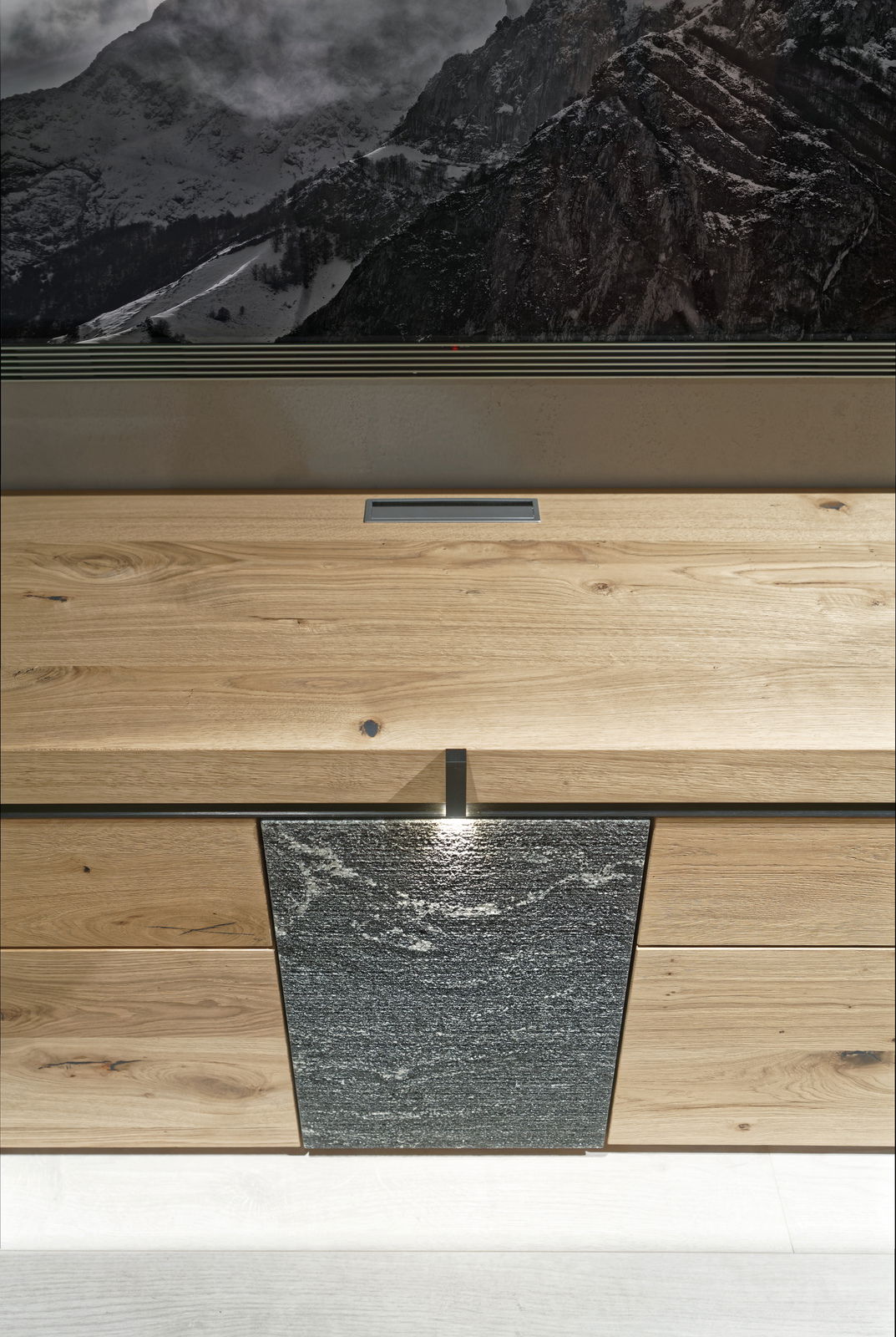 Frontale Ansicht einer Wohnwand mit Holz- und Steinelementen, darunter eine Schublade und eine Tür mit Beleuchtung.