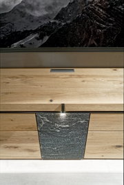 Frontale Ansicht einer Wohnwand mit Holz- und Steinelementen, darunter eine Schublade und eine Tür mit Beleuchtung.