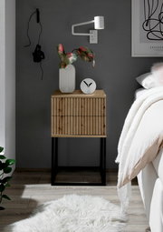 Moderne Nachtkommode aus Holz mit vertikalen Streifen, schwarzem Metallgestell, dekoriert mit einer Vase und einer Uhr, seitliche Perspektive.