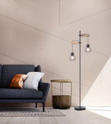 Moderne Stehleuchte aus schwarzem Metall mit zwei Käfiglampen, seitliche Perspektive im Wohnzimmer neben einem Sofa und Beistelltisch.
