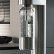 Nahaufnahme einer modernen Wasserflasche in einem Wassersprudler, gefüllt mit sprudelndem Wasser, in einer stilvollen Küchenumgebung.