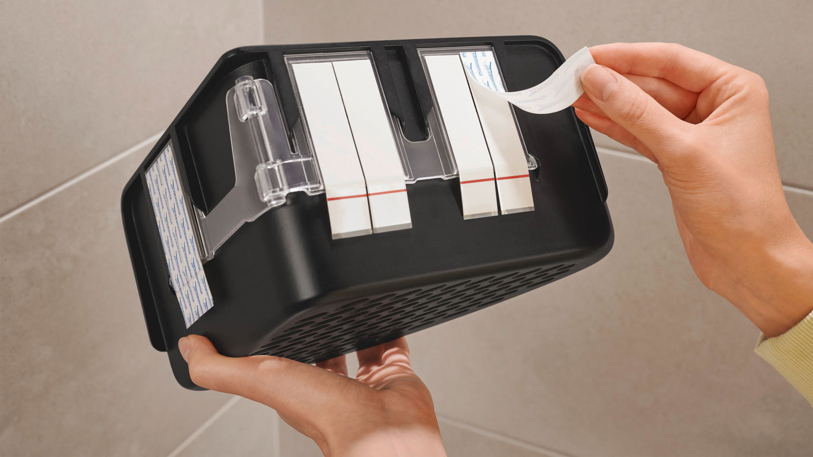 Nahaufnahme eines schwarzen Eckduschkorbs von unten, der mit Klebestreifen an der Wand befestigt wird.