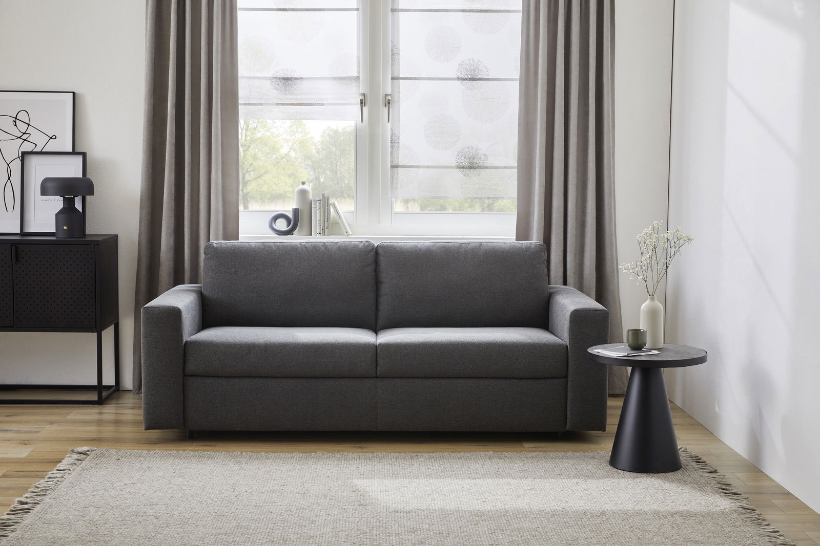 Graues Funktionssofa in einem modernen Wohnzimmer, frontal fotografiert, mit einem Beistelltisch und Dekorationen.