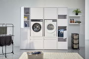Frontansicht eines modernen Waschmaschinenschranks mit integrierter Waschmaschine und Trockner, umgeben von Regalen und Aufbewahrungsmöglichkeiten.