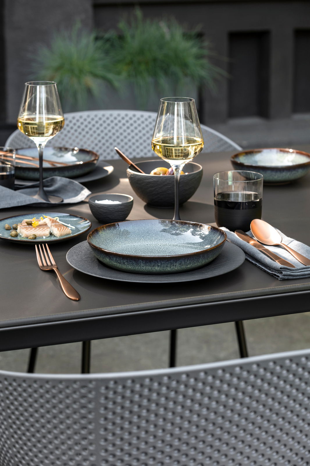 Villeroy & Boch Weißweinkelch-Set 4tlg. Manufacture Rock Glass Elegante Tischdekoration mit zwei Weißweingläsern, gedecktem Tisch und moderner Geschirr- und Besteckauswahl, seitliche Perspektive.