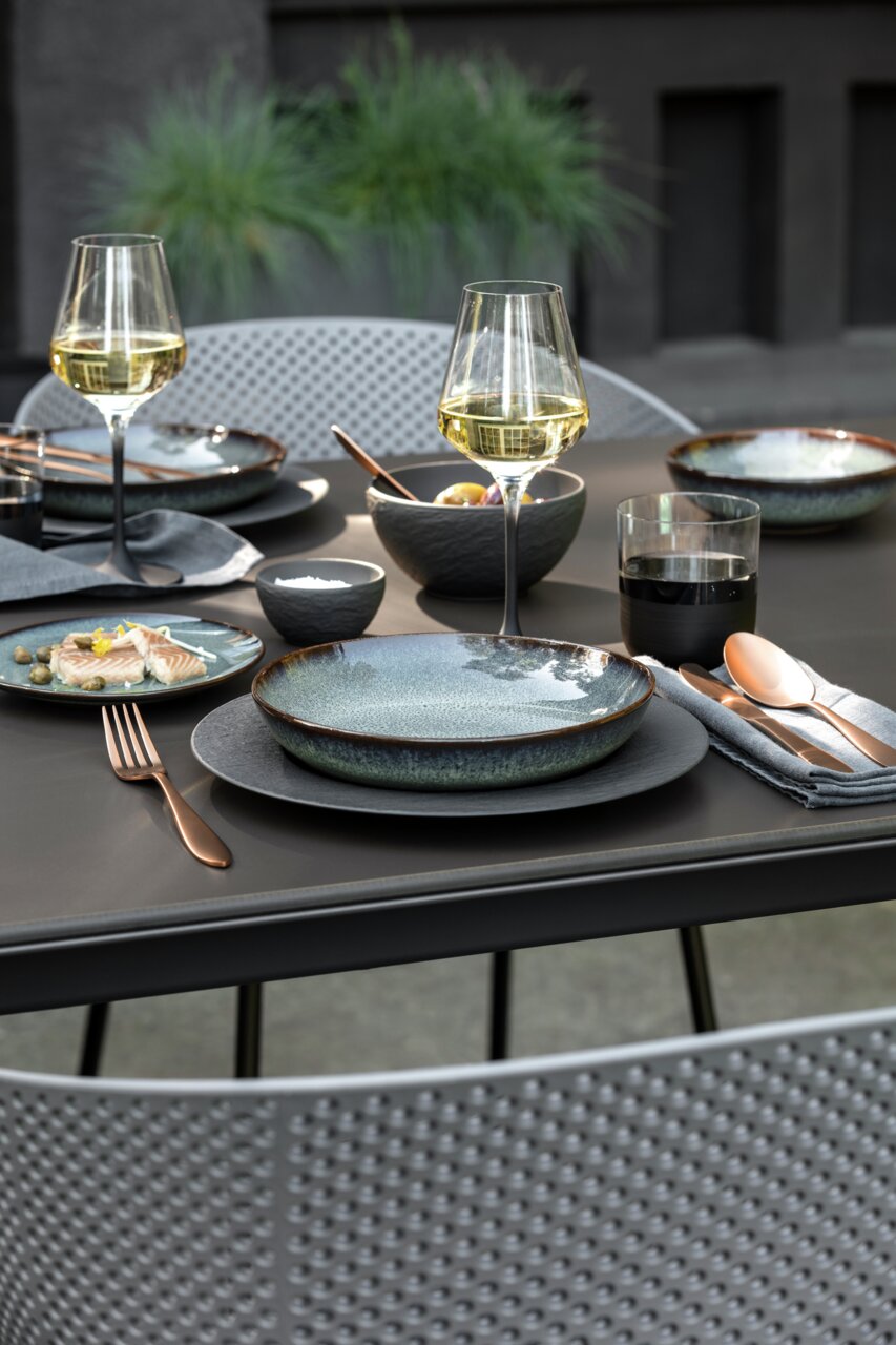 Elegante Tischdekoration mit zwei Weißweingläsern, gedecktem Tisch und moderner Geschirr- und Besteckauswahl, seitliche Perspektive.