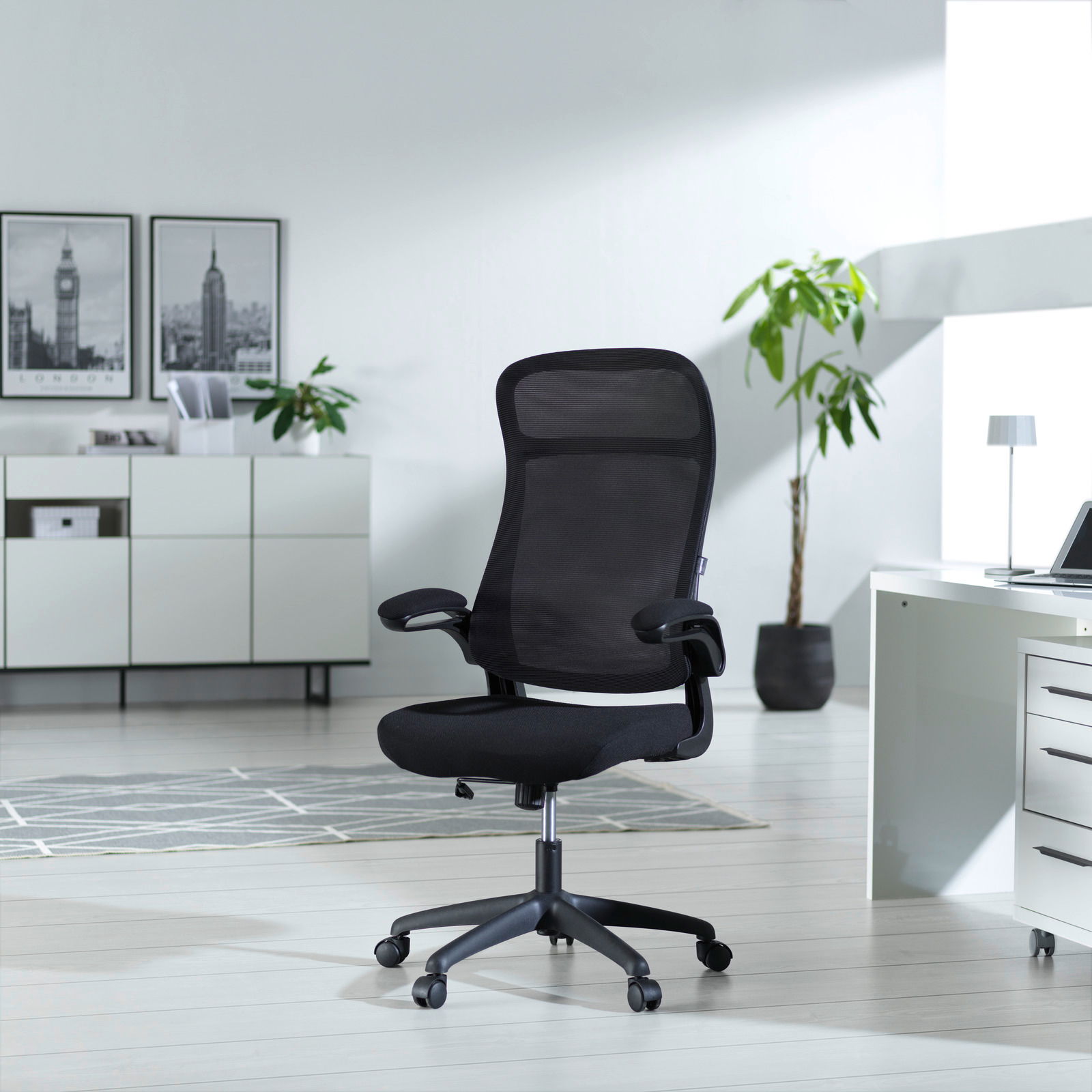 Moderner schwarzer Drehstuhl mit Netzrückenlehne und Armlehnen, seitliche Perspektive in einem hellen Büro mit Pflanzen und Dekoration.