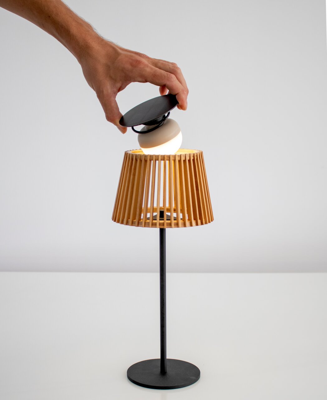 Solar-Tischleuchte mit Holzlamellen und schwarzem Sockel, von der Seite betrachtet, während eine Hand das Solarmodul einsetzt.
