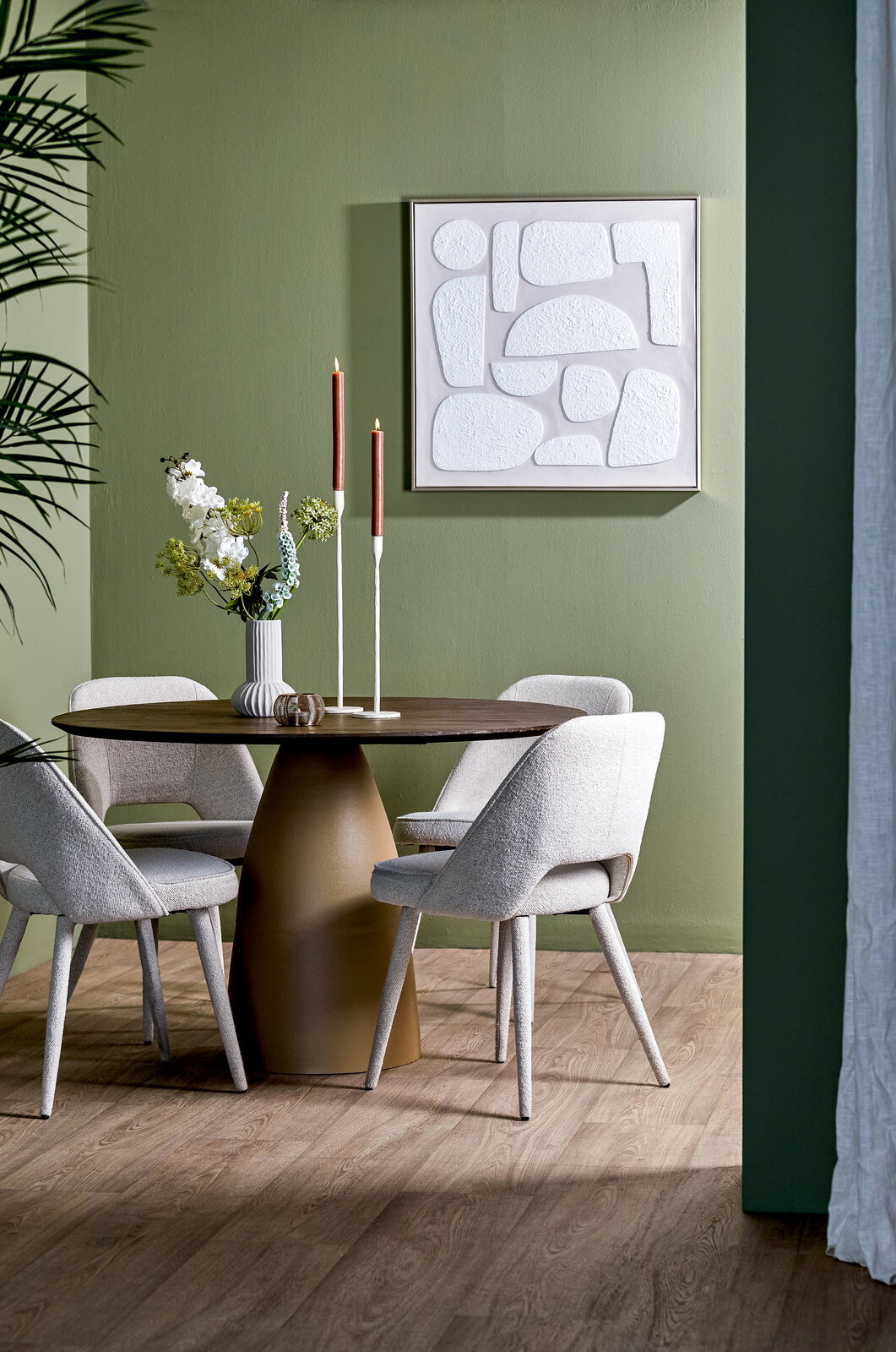 Moderner Esstisch mit runder Tischplatte und konischem Sockel, umgeben von vier gepolsterten Stühlen in einem stilvoll eingerichteten Raum mit grüner Wand und Kunstwerk. Perspektive: seitlich.