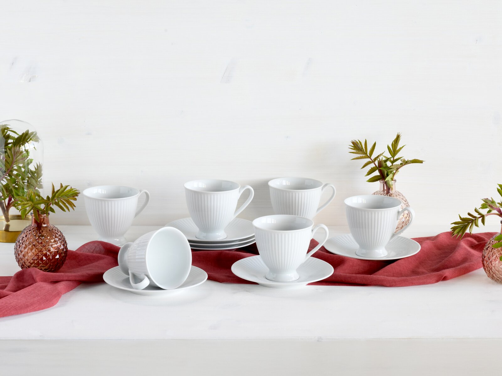 Creatable Kaffeeset 12-tlg VALENCIA Weißes geriffeltes Kaffeetassen-Set mit Untertassen, arrangiert auf rotem Stofftuch auf hellem Tisch, seitliche Frontansicht.