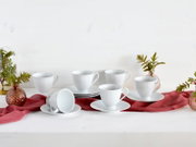 Weißes geriffeltes Kaffeetassen-Set mit Untertassen, arrangiert auf rotem Stofftuch auf hellem Tisch, seitliche Frontansicht.