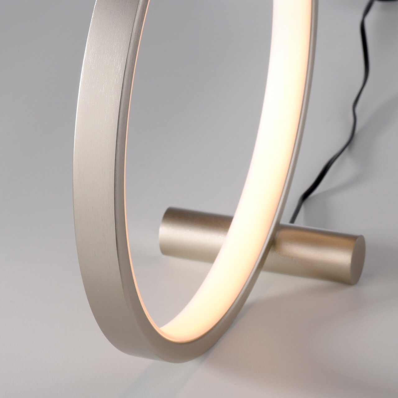 Nahaufnahme einer modernen Tischleuchte MINI RITUS in Ringform mit warmem Licht, seitliche Perspektive