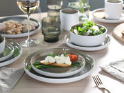 Ein stilvoll gedeckter Tisch mit einem 16-teiligen Kombiservice in Sandfarbe, bestehend aus Tellern, Schalen und Tassen. Im Vordergrund ein Teller mit Brot, Frischkäse und Gemüse. Perspektive von oben.