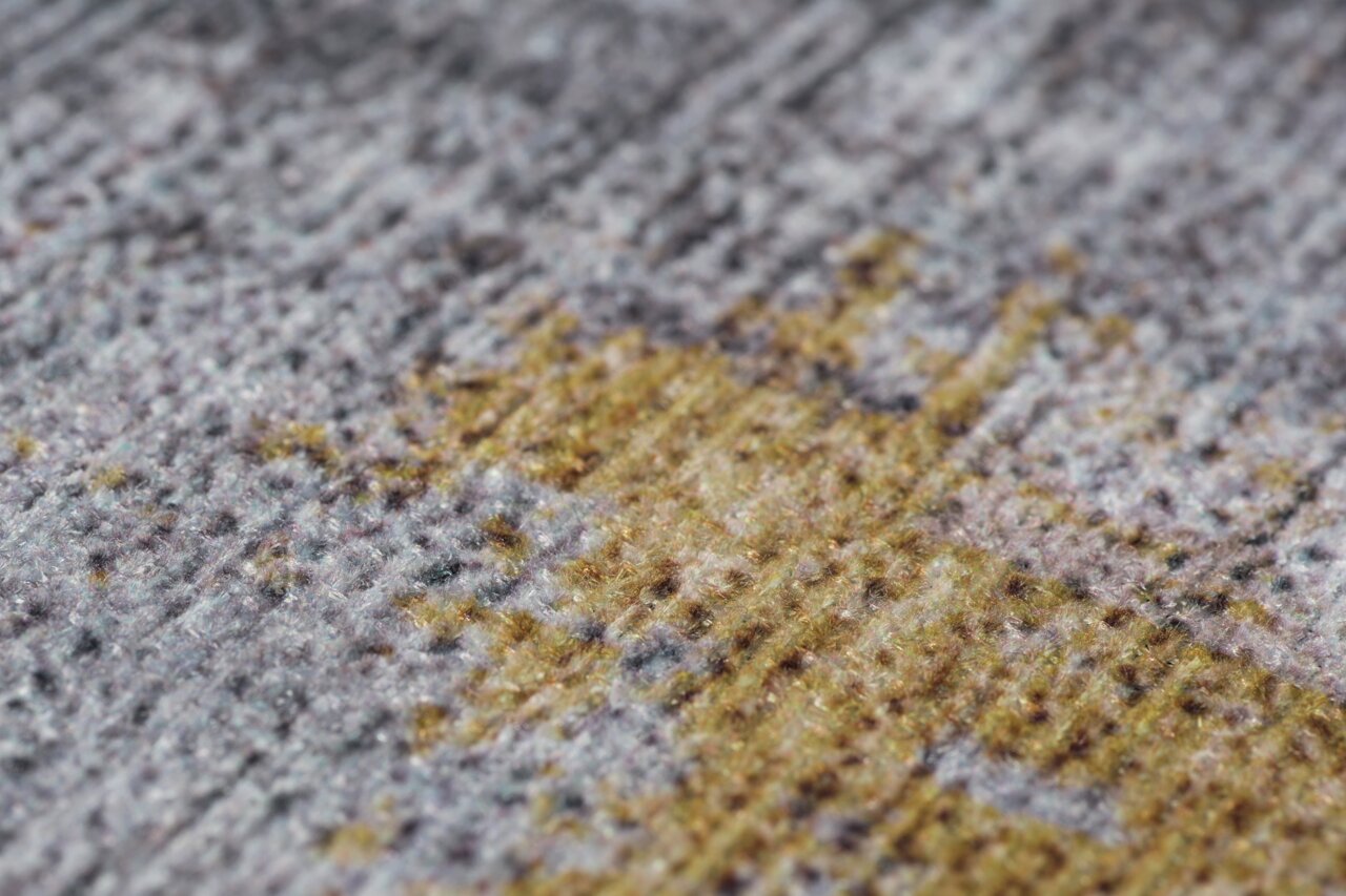 Nahaufnahme eines Teppichs mit einem Muster in Grau- und Gelbtönen, aus seitlicher Perspektive aufgenommen.