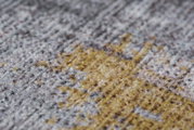 Close-up van een tapijt met een patroon in grijze en gele tinten, gefotografeerd vanuit een zijdelingse hoek.