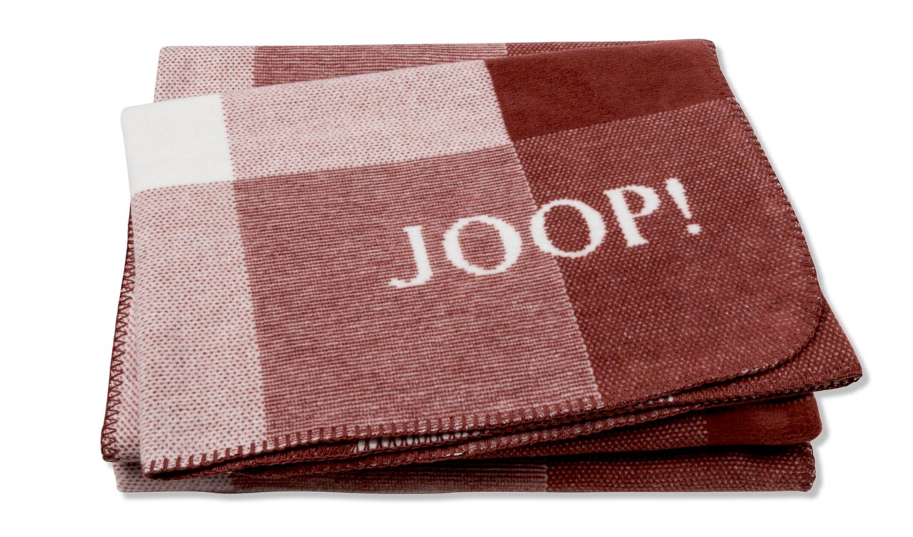 JOOP! Wohndecke J! Mesh Gefaltete Decke mit Karomuster in Rot- und Weißtönen, mit dem Schriftzug 'JOOP!' in der Mitte, aus der Vogelperspektive fotografiert.