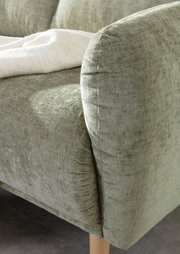 Nahaufnahme einer grünen Sofaecke mit weicher Textur und Holzbeinen, von der Seite fotografiert.