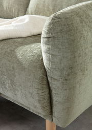 Nahaufnahme einer grünen Sofaecke mit weicher Textur und Holzbeinen, von der Seite fotografiert.