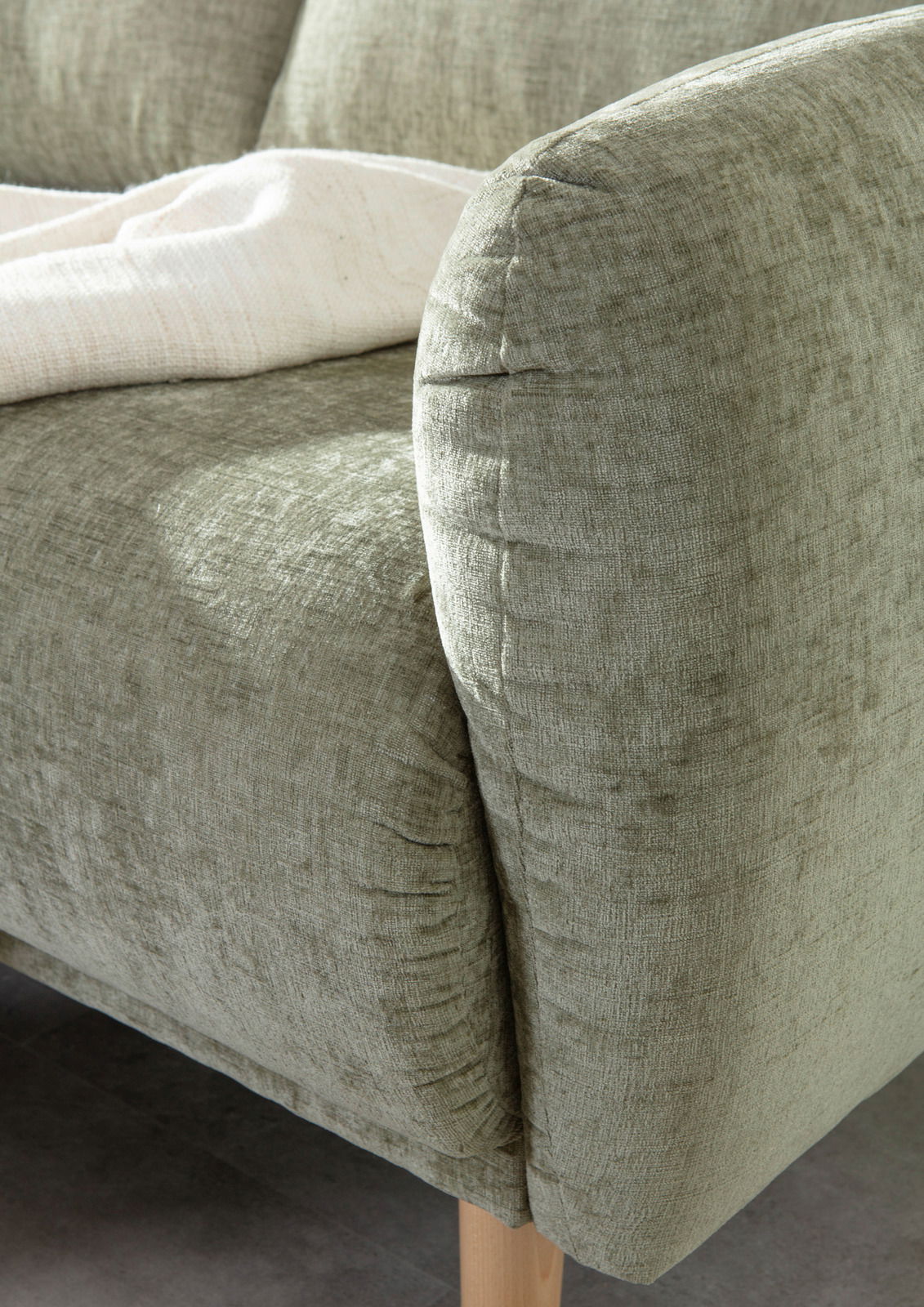 Nahaufnahme einer grünen Sofaecke mit weicher Textur und Holzbeinen, von der Seite fotografiert.