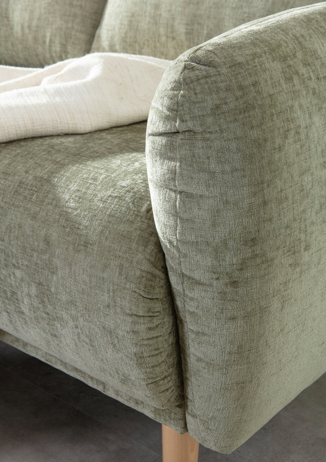Nahaufnahme einer grünen Sofaecke mit weicher Textur und Holzbeinen, von der Seite fotografiert.