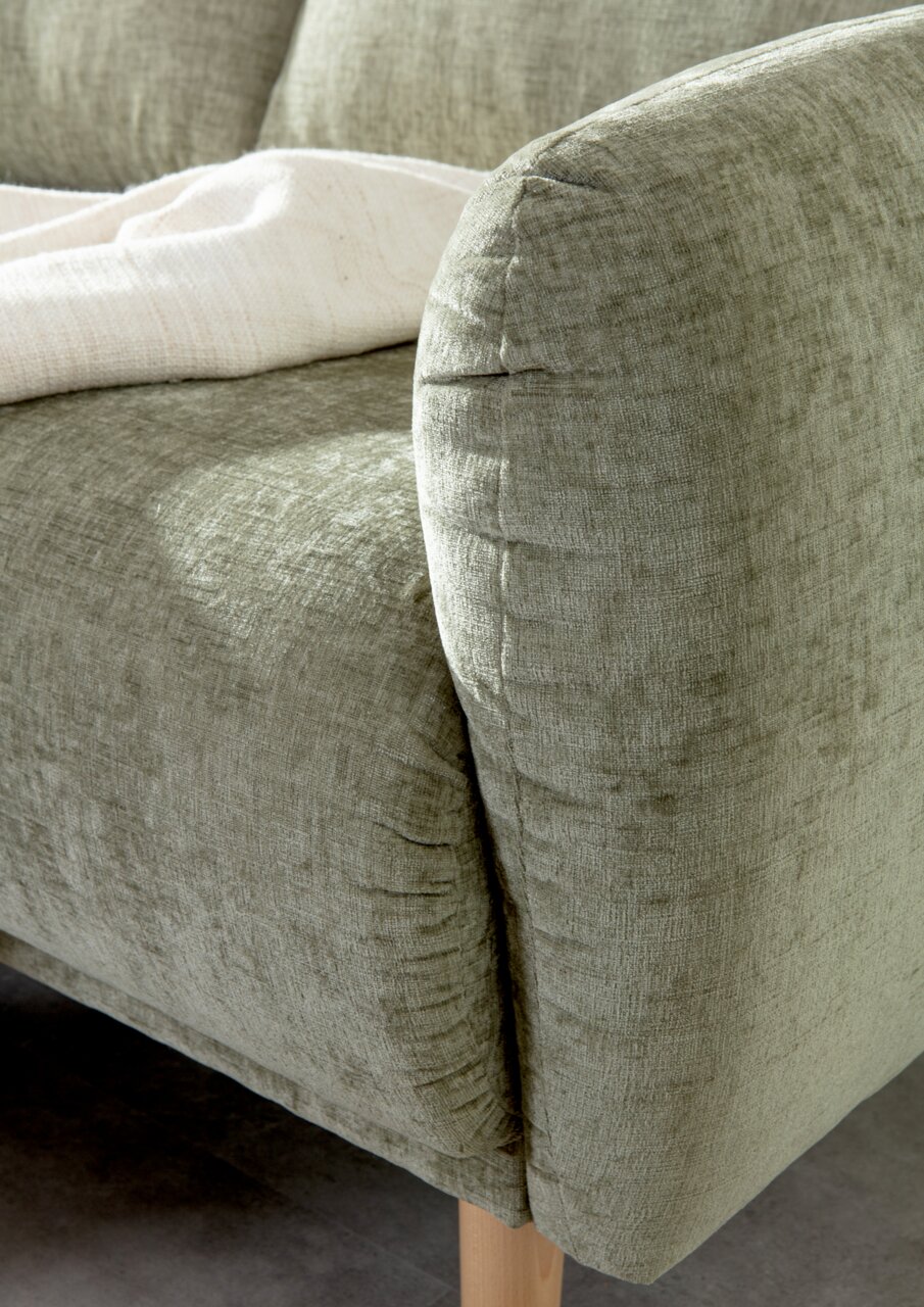Nahaufnahme einer grünen Sofaecke mit weicher Textur und Holzbeinen, von der Seite fotografiert.