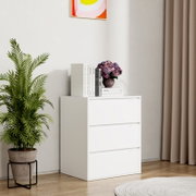 Weiße, moderne Kommode mit drei Schubladen in einer hellen Zimmerecke, oben mit Büchern und Blumenvase dekoriert; Frontansicht in leichter Schrägperspektive von links.