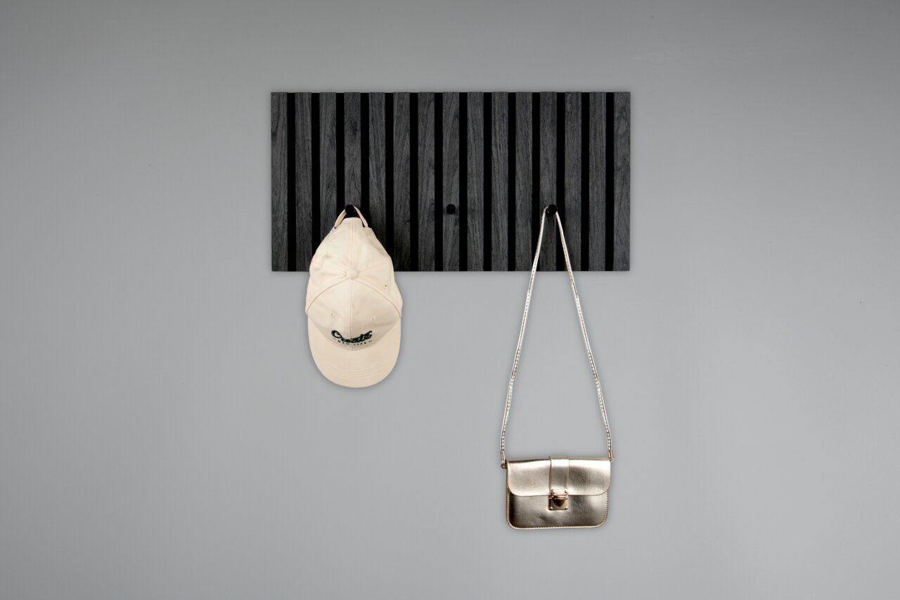 Schwarze Garderobenleiste mit vertikalen Streifen, frontal fotografiert, mit einer weißen Kappe und einer silbernen Tasche daran hängend.