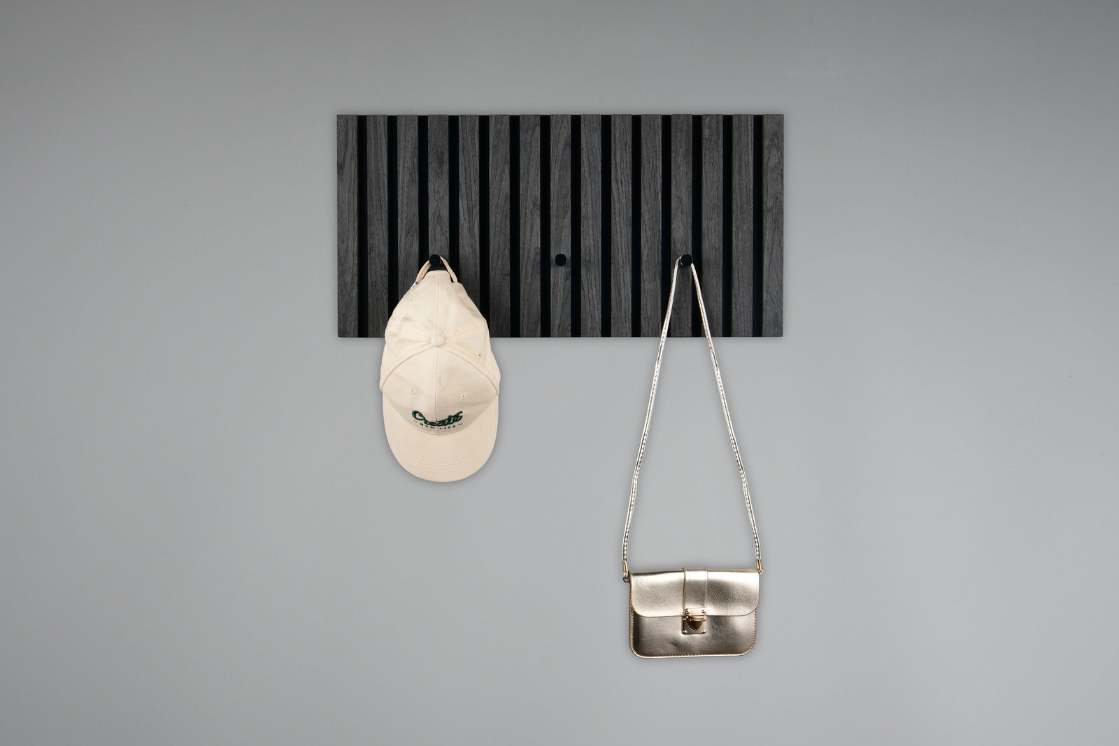Schwarze Garderobenleiste mit vertikalen Streifen, frontal fotografiert, mit einer weißen Kappe und einer silbernen Tasche daran hängend.