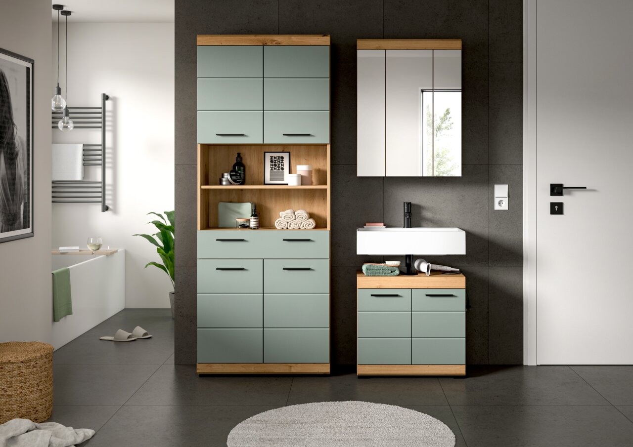 Modernes Badezimmermöbel-Set in Salbeigrün mit Holzakzenten: hoher Hochschrank mit offenen Regalfächern und Unterschrank mit weißem Aufsatzwaschbecken sowie Spiegelschrank an dunkler Wand, Frontansicht.