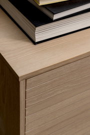 Nahaufnahme eines Sideboards aus hellem Holz mit gestapelten Büchern darauf, von oben betrachtet.