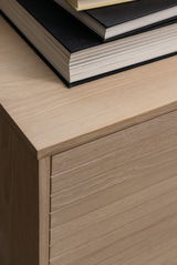 Nahaufnahme eines Sideboards aus hellem Holz mit gestapelten Büchern darauf, von oben betrachtet.