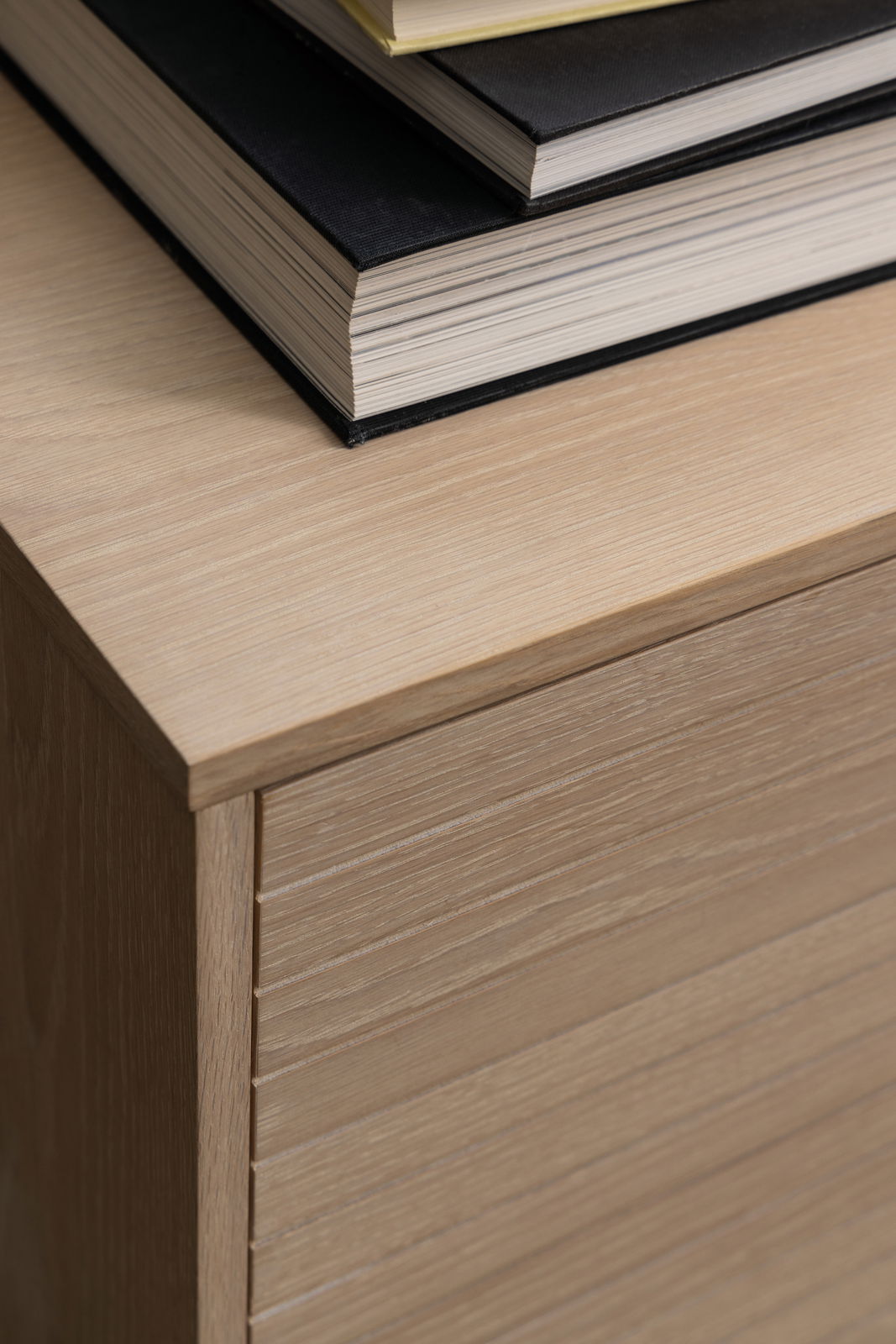 Nahaufnahme eines Sideboards aus hellem Holz mit gestapelten Büchern darauf, von oben betrachtet.