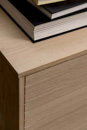 Close-up van een dressoir van licht hout met daarop een stapel boeken, gezien van bovenaf.