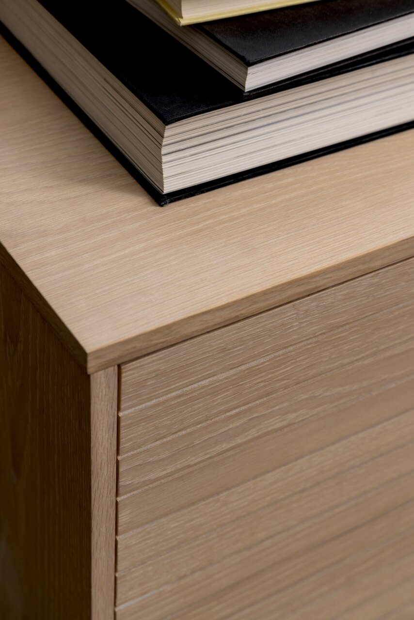 Close-up van een dressoir van licht hout met daarop een stapel boeken, gezien van bovenaf.