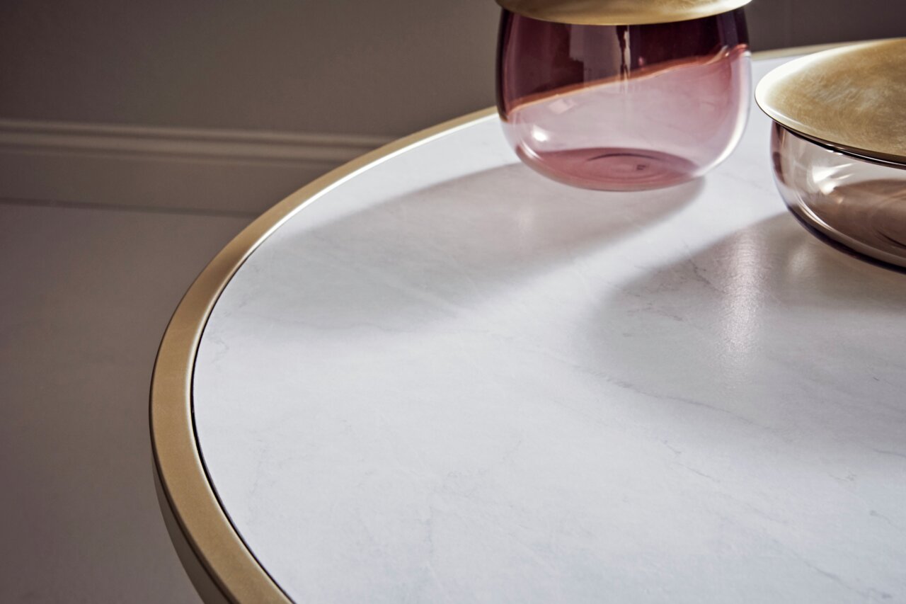 Nahaufnahme eines Couchtischs mit weißer Marmoroptik und goldener Umrandung, darauf stehen zwei dekorative Glasgefäße. Perspektive von oben.